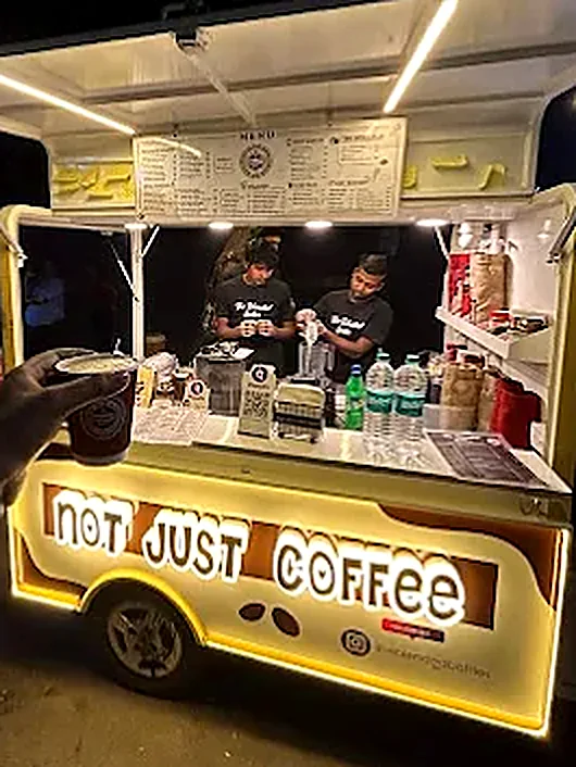 The Blended Bottles cart lit up at night, menu board overhead and the Not Just Coffee sign glowing on the front