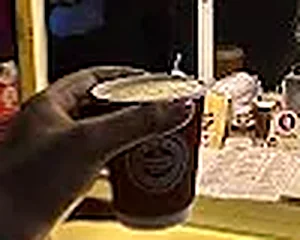 A cold coffee in a branded cup being handed across the counter
